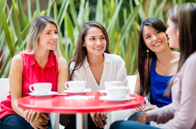 Group of 4 smiling women sitting a table with cups in front of them 