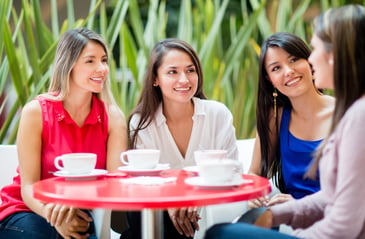 Group of 4 smiling women sitting a table with cups in front of them 